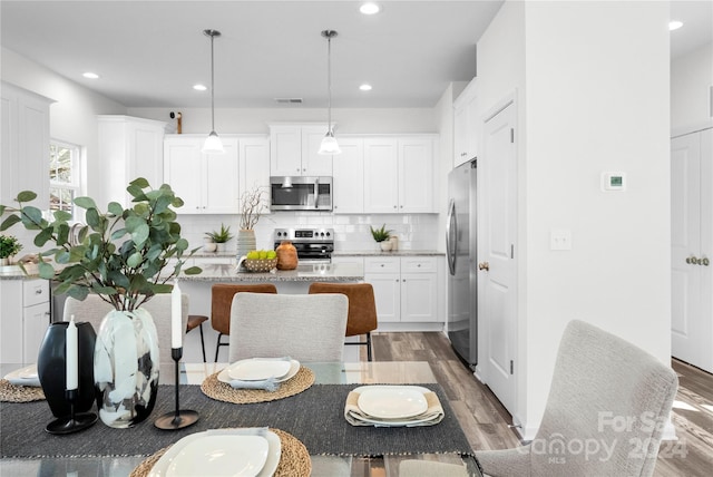 kitchen featuring appliances with stainless steel finishes, pendant lighting, white cabinetry, and hardwood / wood-style floors