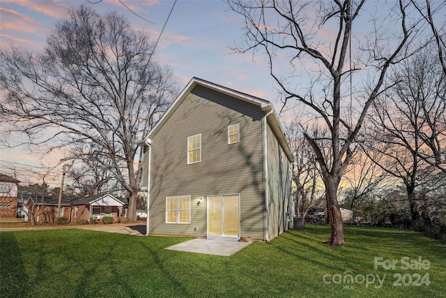 back house at dusk featuring a lawn and a patio