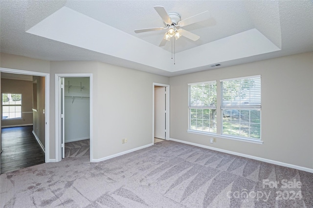 unfurnished bedroom with a spacious closet, ceiling fan, a closet, a tray ceiling, and carpet floors