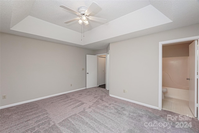 unfurnished bedroom with ceiling fan, a raised ceiling, a textured ceiling, light carpet, and ensuite bath