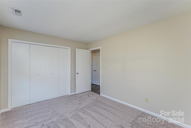 unfurnished bedroom featuring light carpet, a closet, and a textured ceiling