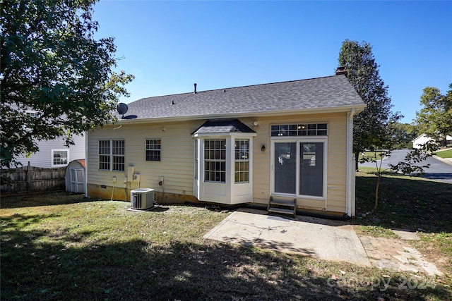 back of house featuring cooling unit, a storage shed, and a lawn