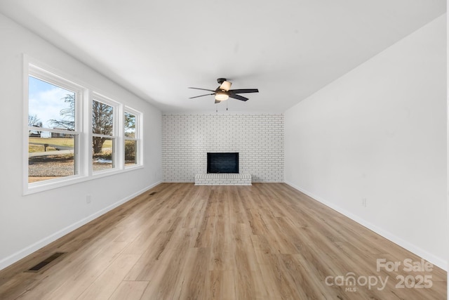 unfurnished living room with a brick fireplace, light hardwood / wood-style flooring, ceiling fan, and brick wall