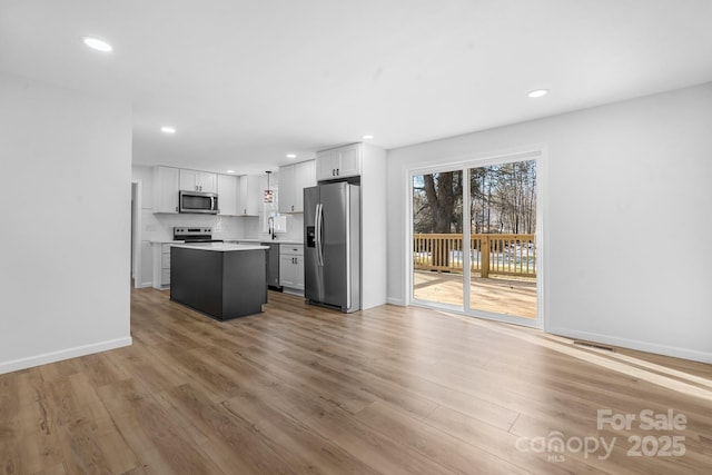 kitchen featuring tasteful backsplash, a kitchen island, stainless steel appliances, light hardwood / wood-style floors, and white cabinets