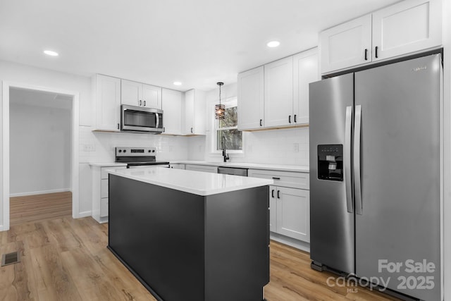 kitchen with a kitchen island, appliances with stainless steel finishes, decorative light fixtures, white cabinets, and light hardwood / wood-style floors