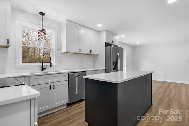 kitchen featuring sink, backsplash, stainless steel appliances, a kitchen island, and decorative light fixtures