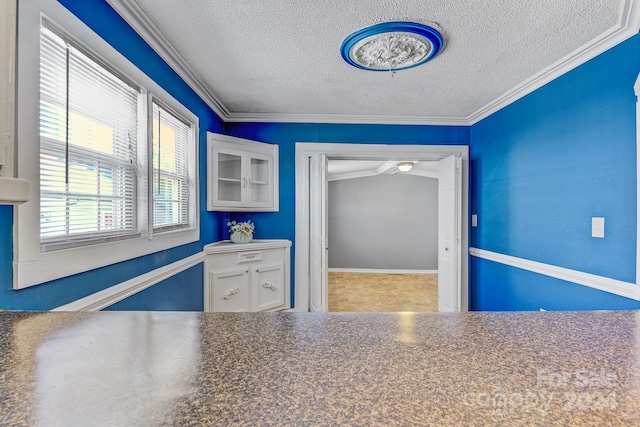 kitchen with white cabinets, a textured ceiling, and crown molding