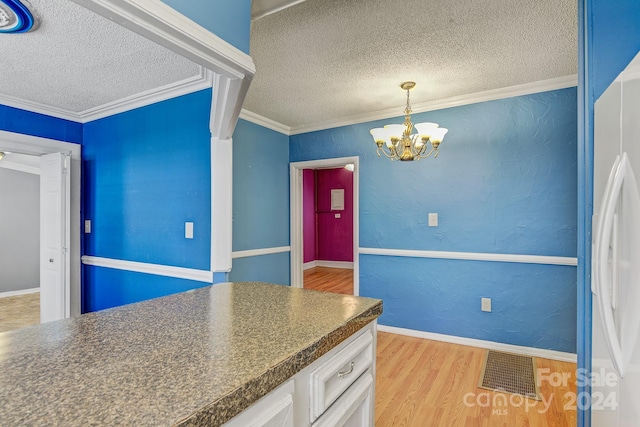 kitchen featuring white refrigerator, a chandelier, light hardwood / wood-style flooring, ornamental molding, and white cabinets