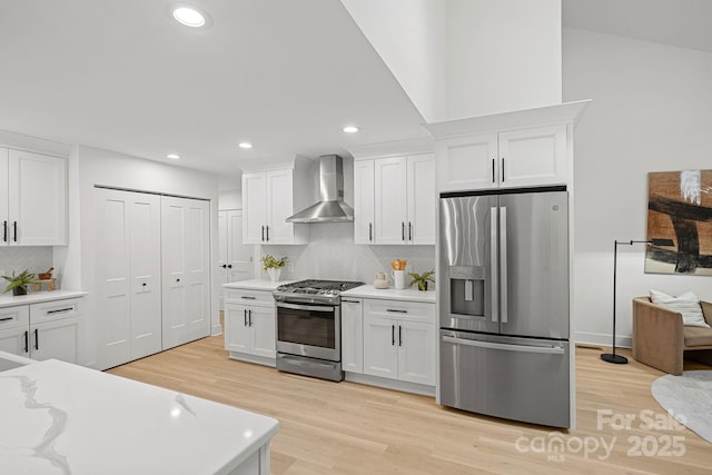 kitchen featuring white cabinetry, wall chimney exhaust hood, light wood-type flooring, tasteful backsplash, and appliances with stainless steel finishes