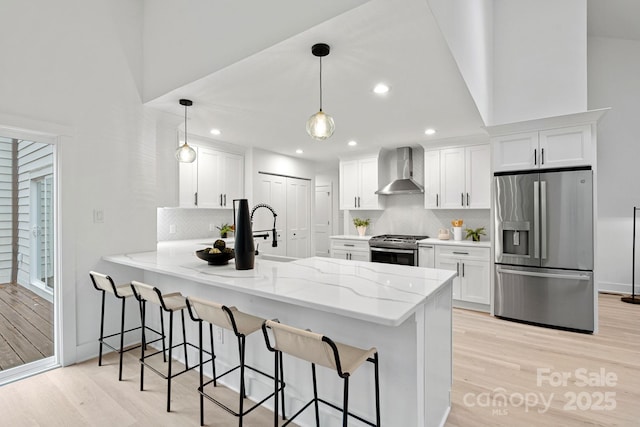 kitchen featuring white cabinets, kitchen peninsula, wall chimney range hood, pendant lighting, and appliances with stainless steel finishes