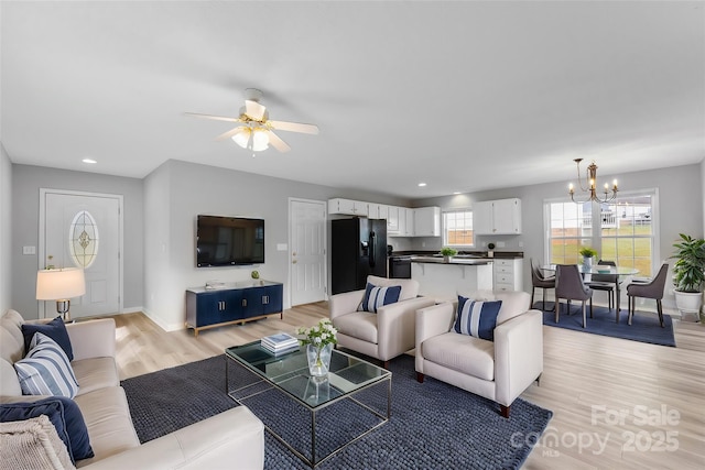 living area with recessed lighting, light wood-style flooring, baseboards, and ceiling fan with notable chandelier