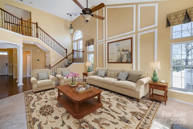 carpeted living room featuring a towering ceiling, decorative columns, and ceiling fan