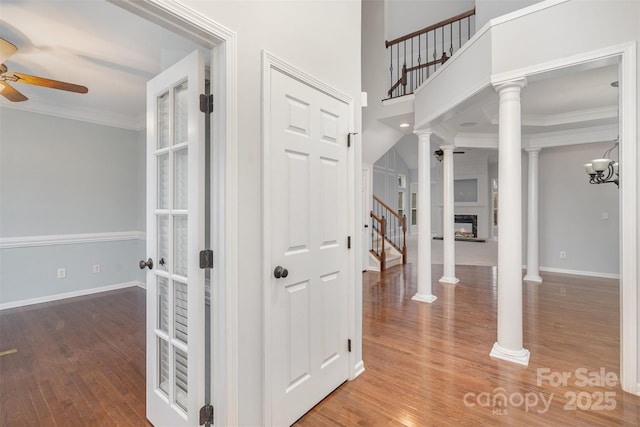 interior space with a ceiling fan, a glass covered fireplace, wood finished floors, crown molding, and ornate columns