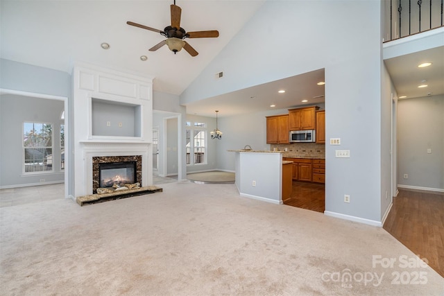 unfurnished living room featuring ceiling fan, high vaulted ceiling, light carpet, a premium fireplace, and visible vents