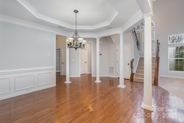 unfurnished dining area with wood finished floors, visible vents, stairs, a tray ceiling, and ornate columns