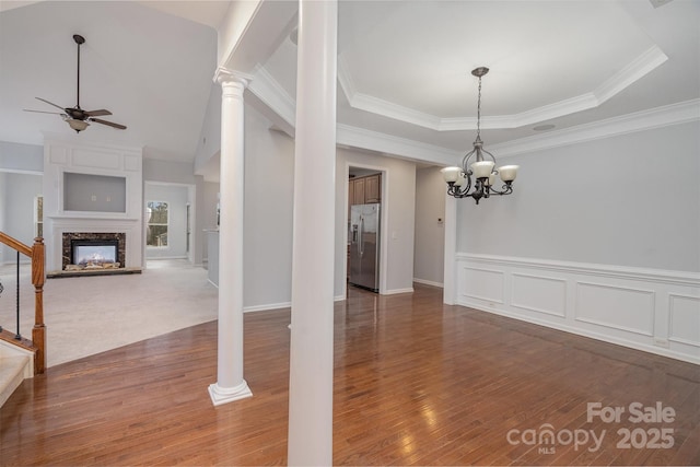 unfurnished dining area featuring a tray ceiling, stairway, a premium fireplace, dark wood-type flooring, and ceiling fan with notable chandelier