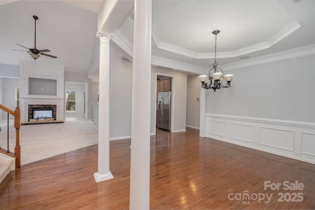 unfurnished dining area featuring a raised ceiling, dark wood finished floors, stairway, a fireplace, and ceiling fan with notable chandelier