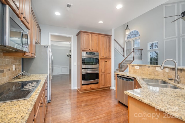 kitchen featuring tasteful backsplash, light stone counters, stainless steel appliances, light wood-style floors, and a sink