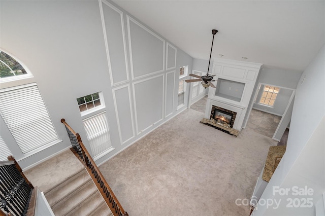 living area featuring a glass covered fireplace, light colored carpet, ceiling fan, and a decorative wall