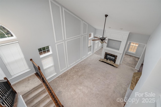 living room featuring a premium fireplace, stairway, a ceiling fan, and light colored carpet