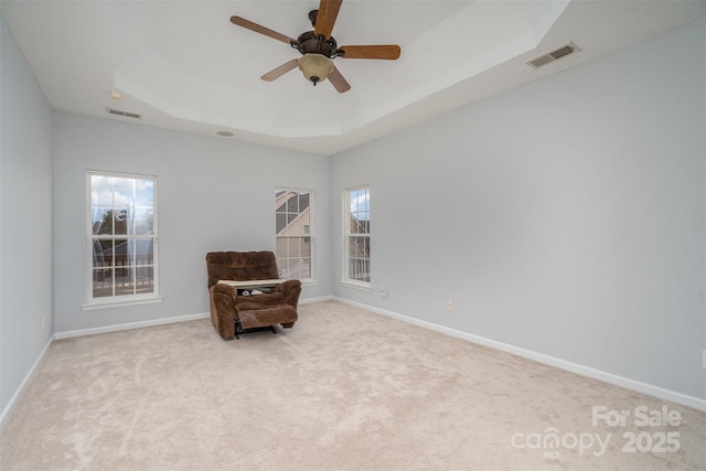 living area with a raised ceiling, visible vents, light carpet, and baseboards