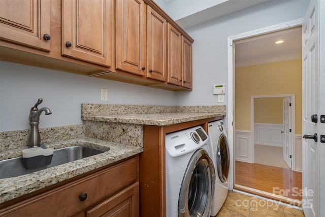 washroom with cabinet space, a decorative wall, washing machine and dryer, wainscoting, and a sink