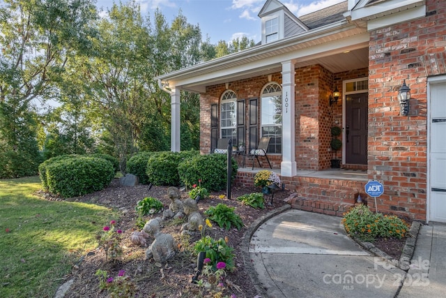 entrance to property with a porch, a yard, and brick siding