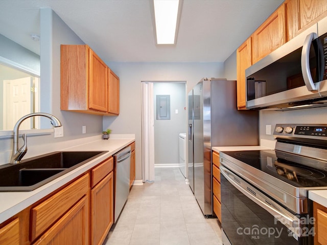 kitchen featuring electric panel, light tile patterned floors, appliances with stainless steel finishes, washing machine and clothes dryer, and sink