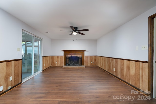 unfurnished living room with a brick fireplace, wooden walls, dark hardwood / wood-style flooring, and ceiling fan