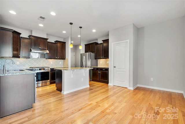 kitchen featuring sink, appliances with stainless steel finishes, a kitchen breakfast bar, a kitchen island, and decorative light fixtures