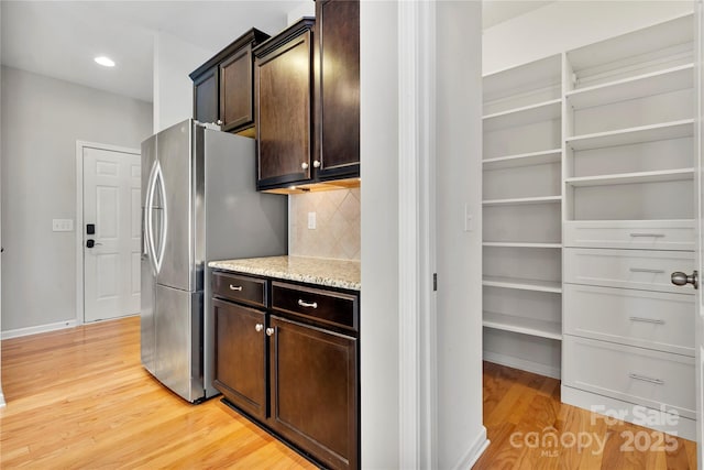 kitchen with dark brown cabinetry, backsplash, stainless steel refrigerator with ice dispenser, and light wood-type flooring