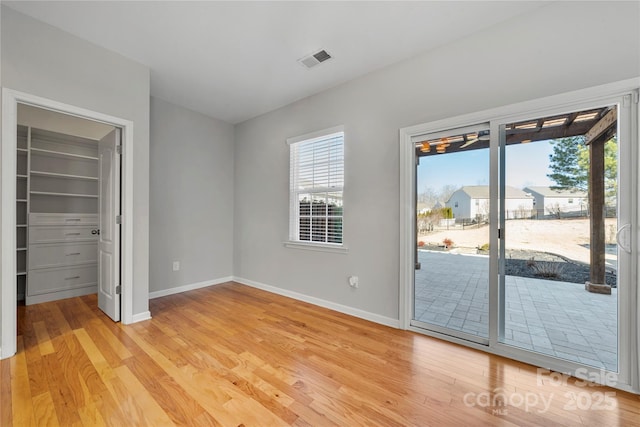 unfurnished bedroom featuring access to exterior, a spacious closet, light hardwood / wood-style floors, and a closet