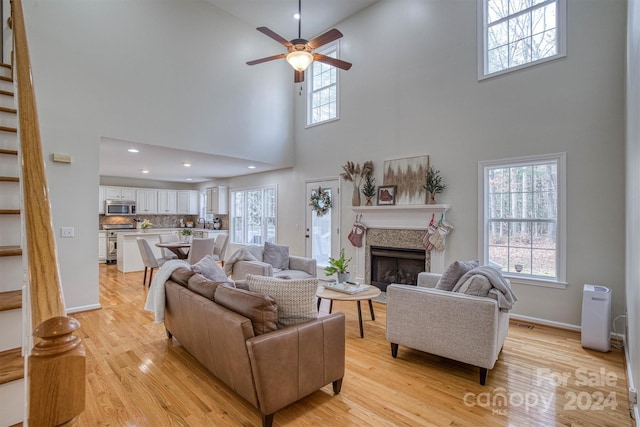 living room featuring ceiling fan, a towering ceiling, and light hardwood / wood-style flooring