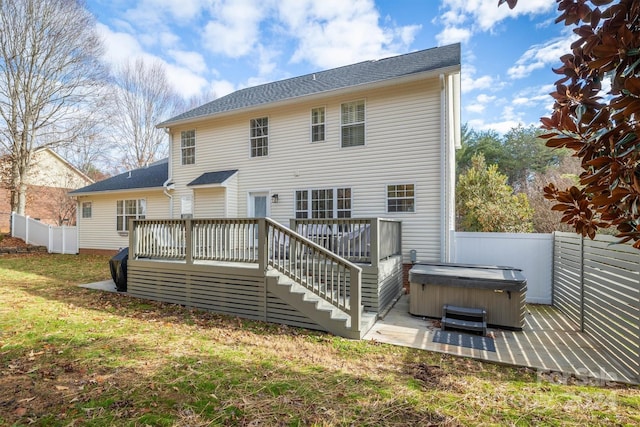 back of property with a hot tub, a deck, and a lawn