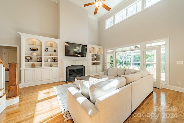 living room with a towering ceiling, crown molding, light hardwood / wood-style floors, and ceiling fan