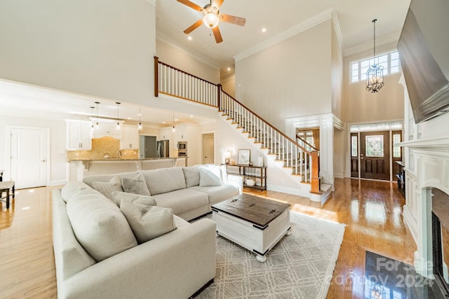 living room with ornamental molding, light hardwood / wood-style floors, ceiling fan with notable chandelier, and a towering ceiling