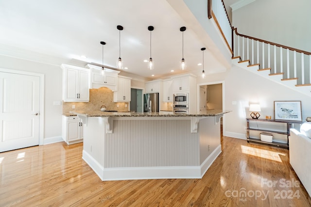 kitchen featuring a kitchen breakfast bar, appliances with stainless steel finishes, white cabinetry, and light hardwood / wood-style floors