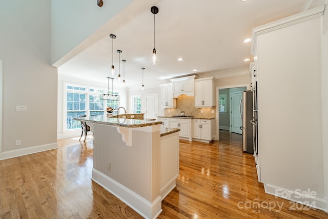 kitchen featuring a kitchen island with sink, hanging light fixtures, a breakfast bar, light wood-type flooring, and white cabinetry