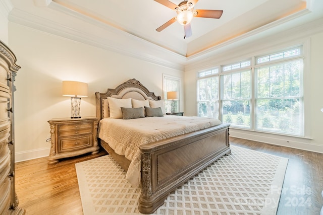 bedroom with a raised ceiling, crown molding, light wood-type flooring, and ceiling fan