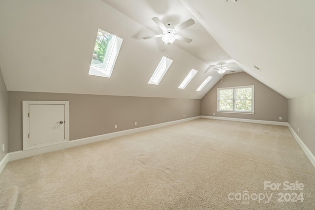 additional living space with vaulted ceiling with skylight, light carpet, and ceiling fan