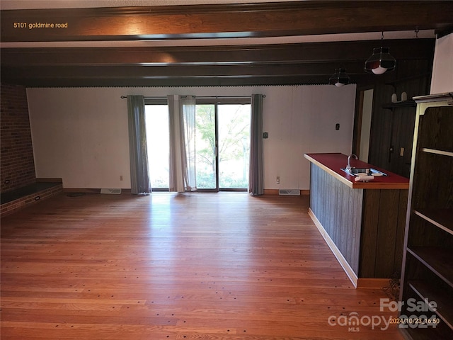 unfurnished living room with hardwood / wood-style flooring, beamed ceiling, and sink