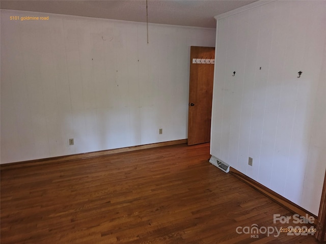 unfurnished room featuring wood walls, ornamental molding, and dark wood-type flooring