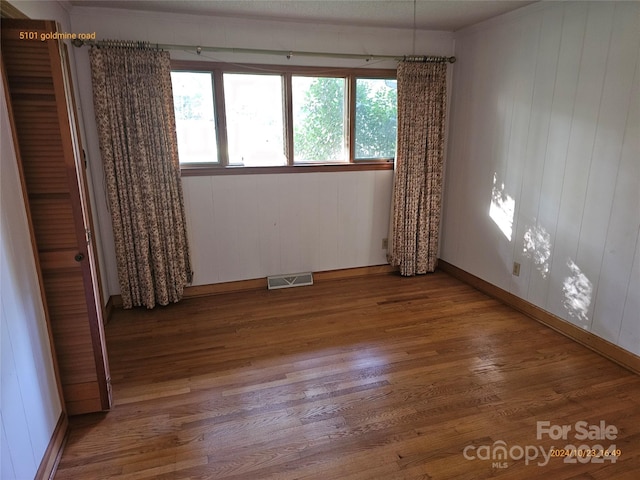 empty room with wood walls, plenty of natural light, and hardwood / wood-style floors