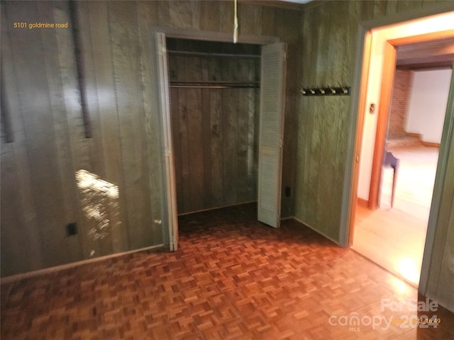 unfurnished bedroom with wood walls, parquet floors, and a closet