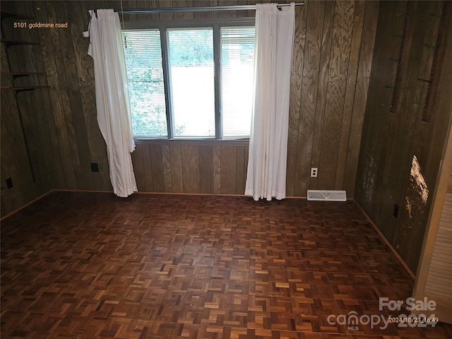 unfurnished room featuring wood walls and dark parquet flooring