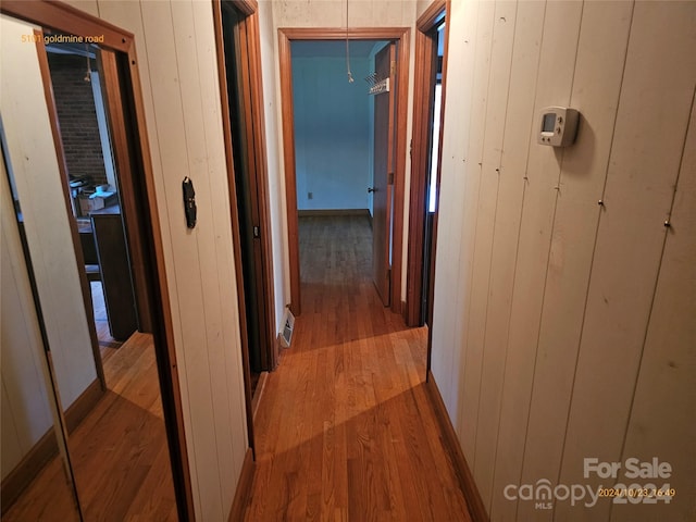 corridor with light wood-type flooring and wood walls