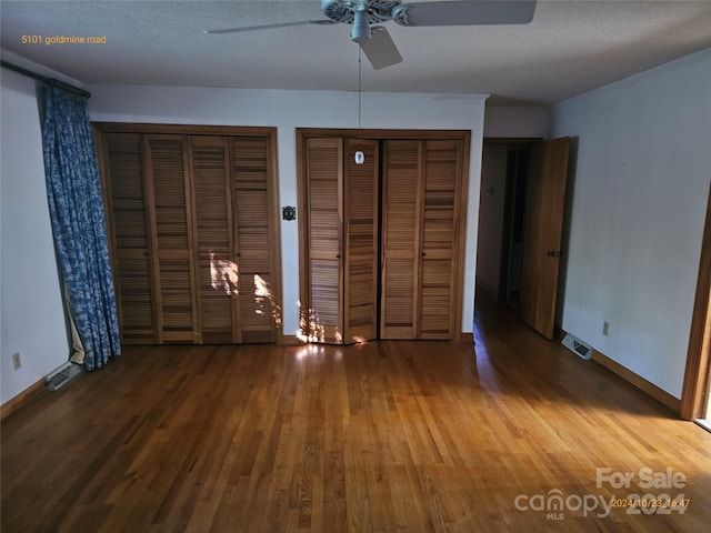 unfurnished bedroom featuring ceiling fan, multiple closets, a textured ceiling, and hardwood / wood-style floors