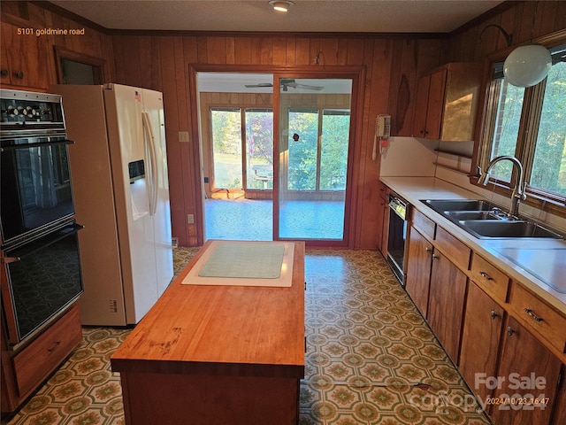 kitchen featuring wooden counters, sink, wooden walls, and black appliances