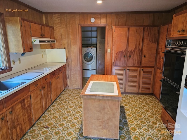 kitchen featuring wood walls, washer / clothes dryer, white stovetop, crown molding, and black double oven