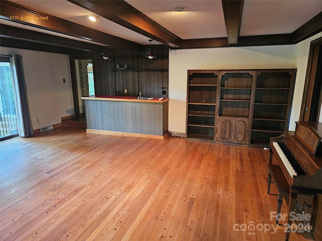 unfurnished living room with beamed ceiling, wooden walls, light wood-type flooring, and plenty of natural light